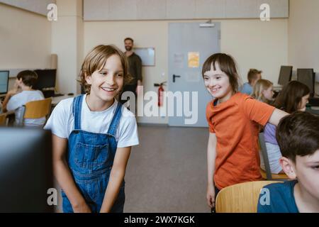 Glückliches Mädchen, das Spaß mit einer behinderten Freundin im Computerunterricht hat Stockfoto