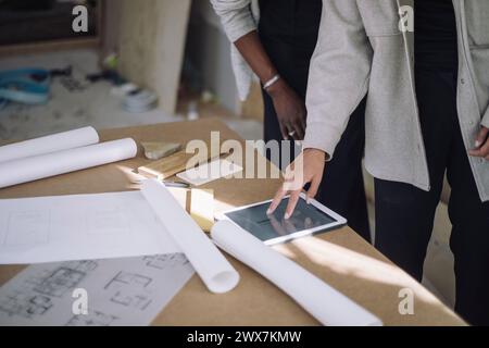 Mitte der Konstrukteurin, die der Kollegin einen Plan über ein digitales Tablet auf dem Tisch bei Under Constr erklärt Stockfoto