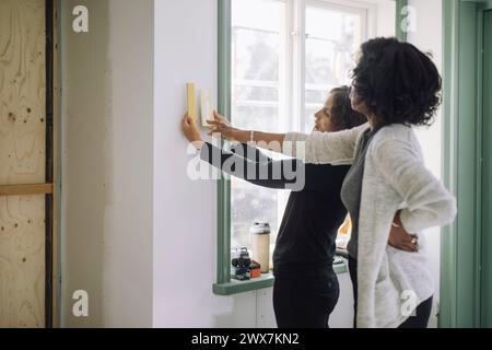 Weibliche Kundin und Architektin wählte die Farbe der Wandfarbe, während sie in der Nähe des Fensters in der im Bau befindlichen Wohnung stand Stockfoto