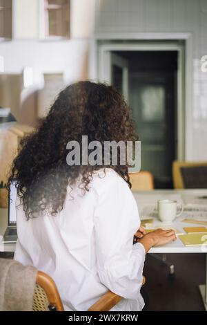 Rückansicht einer Architektin mit lockigem Haar, die im Büro arbeitet Stockfoto