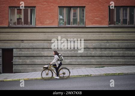 Seitliche Ansicht der Freiberuflerin in voller Länge, die auf der Straße unterwegs ist, während sie durch das Fahrrad in der Stadt pendelt Stockfoto