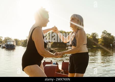 Glückliche ältere Freundinnen, die während des Urlaubs Hände halten und auf dem Hausboot tanzen Stockfoto