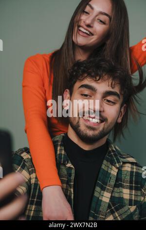 Positives junges Ostpaar, das ein lässiges Outfit trägt und ein Smartphone benutzt, um ein Video zu streamen, isolierter Hintergrund. Berühmte Influencer Lady, die Blog aufnimmt Stockfoto