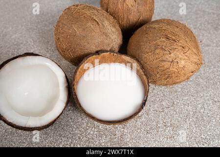Kokosmilch in Kokosnussschale und Kokosnuss, gehacktes Fleisch auf grauem Hintergrund Stockfoto
