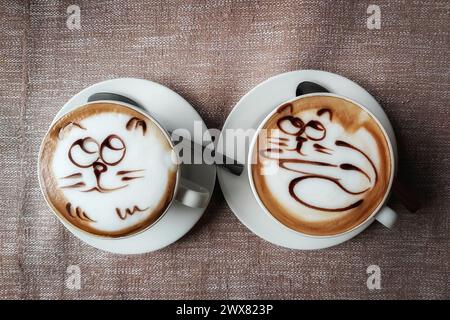 Zwei Tassen duftender Kaffee mit einem Muster auf weißem Schaum, auf einer Untertasse auf einer Tischdecke in einem Stadtcafé. Stockfoto