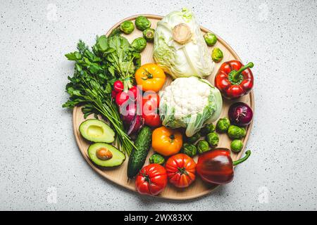 Rustikales Holztablett mit Auswahl an frischem Gemüse und Grün auf weißem Küchentisch mit Blick von oben. Vegetarische und diätetische Lebensmittel aus biologischen Zutaten Stockfoto