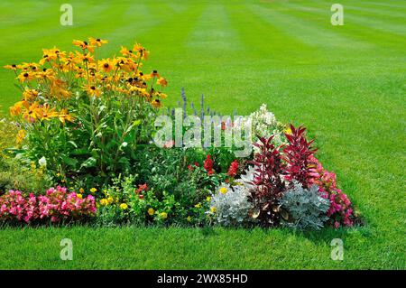 Malerischer Blick auf farbenfrohe Blumenbeete, einen üppigen grünen Rasen und ein gewundenes Gras. Stockfoto