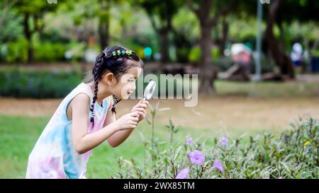 Ein junges Mädchen untersucht Blumen mit einer Lupe Stockfoto