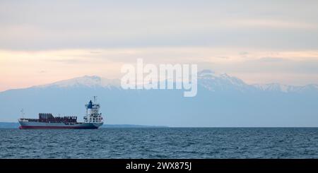 Thessaloniki, Griechenland - 03. Mai 2019: Frachtschiffe im Thermaischen Golf vor dem schneebedeckten Gipfel des Olymp bei Sonnenuntergang vor Anker. Stockfoto