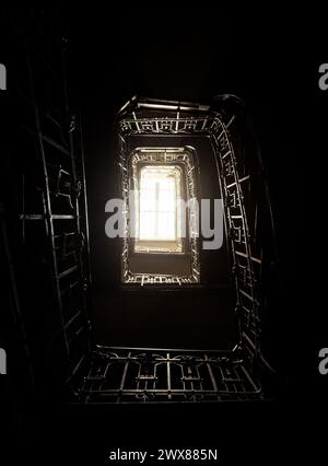 Ich schaue auf die Wendeltreppe im alten Haus. Dunkle Treppe mit Metall-bannister. Raum gefüllt mit Licht aus dem oberen Stockwerk. Stockfoto
