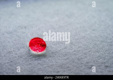 Roter Tropfen Wasser, der aussieht wie ein glühender Stein auf einem Blatt weißen Stoffes. Stockfoto