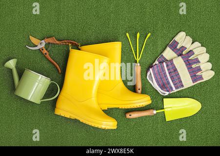 Zusammensetzung mit Gummistiefeln, Gartenwerkzeugen und Handschuhen auf grünem Hintergrund. Draufsicht Stockfoto