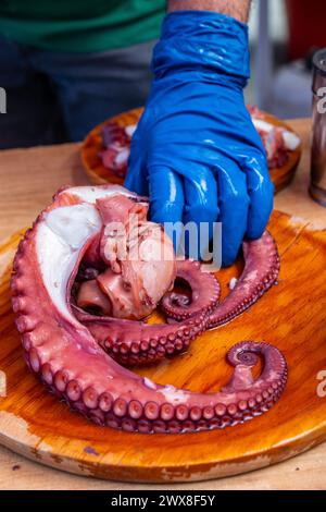 Halten Sie ein paar Tentakel Tintenfisch in der Hand, um ihn zu schneiden, und bereiten Sie einige Portionen von „pulpo a feira“ zu. Stockfoto