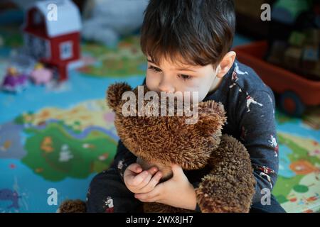 Nachdenklicher Junge, der einen Spielzeugbären im Kinderzimmer umarmt Stockfoto