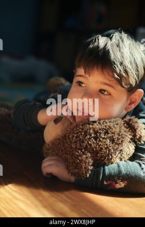 Nachdenklicher Junge, der einen Spielzeugbären im Kinderzimmer umarmt Stockfoto