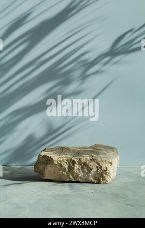 Felsenpodium auf hellgrauem Hintergrund und dem Schatten einer Palme. Natursteinpodium zur Produktpräsentation. Hintergrund für Kosmetik. Stockfoto