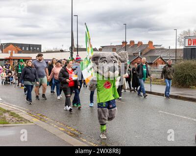 Warrington Rugby League Mascot, Wolfie, weht beim Spaziergang in der St. Patrick's Day Parade 2024 Stockfoto