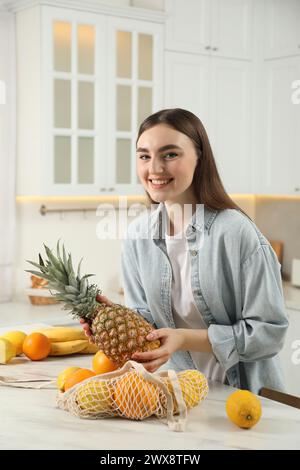 Frau, die Ananas aus der Schnur-Tasche am hellen Marmortisch in der Küche nimmt Stockfoto