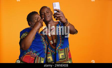 Glückliches afroamerikanisches Paar, das im Studio einen niedlichen Moment festnimmt, Fotos auf dem Smartphone macht und Freizeitaktivitäten genießt. Romantische verheiratete Menschen machen Fotos für Erinnerungen am Telefon. Stockfoto