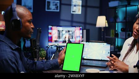 Tablet mit isoliertem Bildschirm vor dem Podcast des Showhosts, der eine nette Unterhaltung mit einem glücklichen Gast genießt. Chroma-Schlüsselgerät im professionellen Studio für Podcasting-Live-Session mit Frau Stockfoto