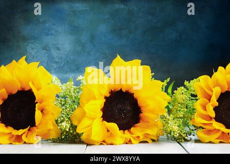 Drei große schöne Sonnenblumen vor blauem malerischem Hintergrund mit Kopierraum. Vorderansicht. Stockfoto