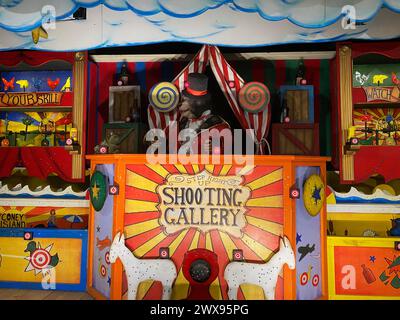 Eine lebendige Fotogalerie im Vintage-Stil bei einem Karneval mit einem Animatronic-Bären, der als karnevalsbarker gekleidet ist und die Teilnehmer einlädt, ihr Ziel zu testen Stockfoto