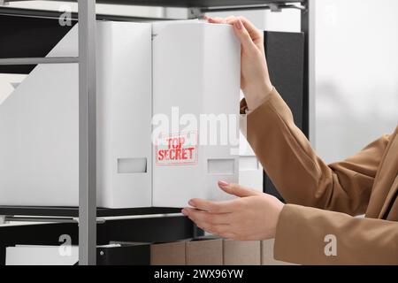 Streng geheimer Stempel. Frau nimmt Aktenmappe mit Dokumenten aus dem Regal drinnen, Nahaufnahme Stockfoto