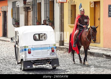 Antigua, Guatemala. März 2024. Ein römischer Centurion auf dem Pferderücken passiert eine Auto-Rikscha während der Veranstaltungen am Heiligen Donnerstag in der Semana Santa, am 28. März 2024 in Antigua, Guatemala. Die opulenten Prozessionen, detailgetreuen Alfombras und jahrhundertealten Traditionen ziehen mehr als 1 Million Menschen in die alte Hauptstadt. Quelle: Richard Ellis/Richard Ellis/Alamy Live News Stockfoto