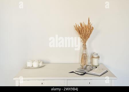 Wunderschöner Blumenstrauß aus getrockneten Pampas-Grasblumen, Schilfblume in einer Glasvase vor weißer Wand, Kerze, geöffnetes Buch. Hintergrund mit Kopierraum, leer. Vorlage, Modell für Design, Poster, Kunst. Stockfoto