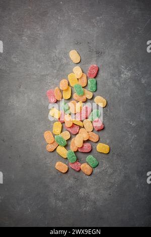 jujubes, bunte gummiartige Bonbons mit Fruchtgeschmack und länglich geformtem verstreuten schwarzen rustikalen strukturierten Hintergrund, Kopierraum von oben Stockfoto