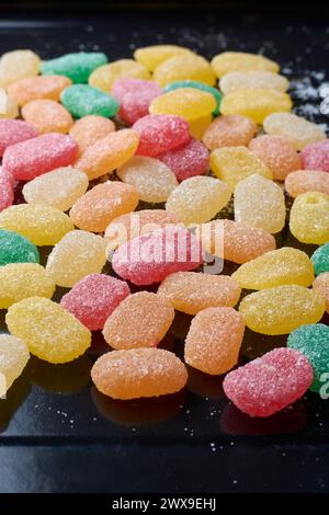 jujubes, bunte gummiartige Bonbons mit Fruchtgeschmack und länglich geformtem, verstreuten schwarzen Hintergrund, weicher Fokus mit Kopierraum Stockfoto