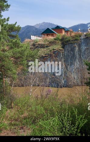 Das Dorf Chemal Altai liegt an einem hohen Felsufer oberhalb des Katun River. Im Vordergrund steht ein mit Bäumen und Büschen bewachsenes Ufer. Im Hintergrund Stockfoto