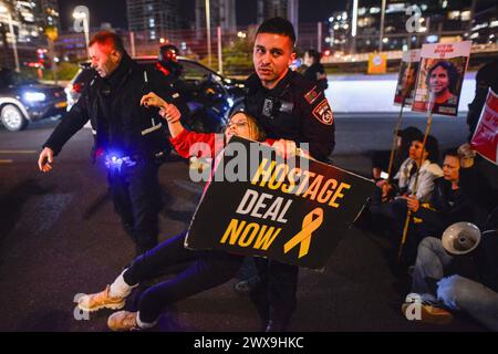 Tel Aviv, Israel. März 2024. Ein israelischer Polizist entfernt einen Demonstranten mit einem Plakat, auf dem steht: "Geiselhandel jetzt" von der blockierten Autobahn Ayalon. Hunderte von Demonstranten schlossen sich Familienmitgliedern der israelischen Geiseln an, um einen sofortigen Geiselvertrag zu fordern. Während des Protestes drangen Familienmitglieder in Metallkäfige ein, die auf der Straße platziert wurden und blockierten anschließend den Ayalon Highway. Quelle: SOPA Images Limited/Alamy Live News Stockfoto