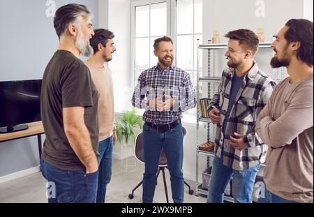 Die Gesellschaft männlicher bärtiger Freunde, die sich unterhalten und lachen und sich zu Hause amüsieren. Stockfoto