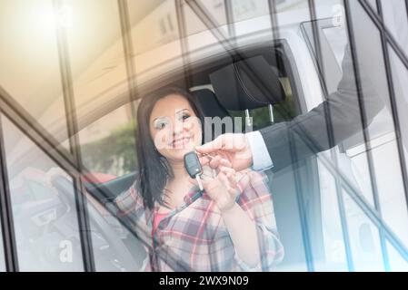 Autoverkäufer gibt der hübschen jungen Frau Autoschlüssel, Lichteffekt; Mehrfachbelichtung Stockfoto