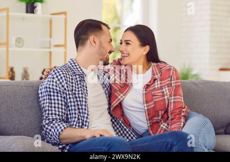 Junge glückliche verheiratete Paare sitzen auf dem Sofa im Wohnzimmer zu Hause und lächeln. Stockfoto