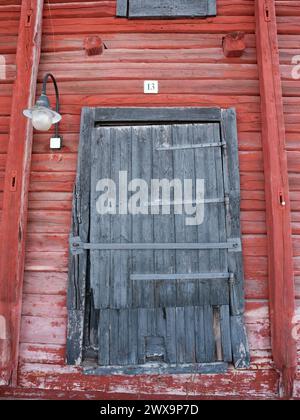 Verschlossene alte Lagertür Nr. 13 des rot lackierten Blockhausgebäudes Stockfoto