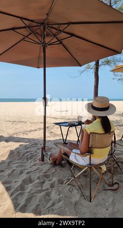 Rayong Thailand 13 März 2024, Eine Frau entspannt sich in einem Stuhl unter einem Sonnenschirm am Sandstrand und genießt die friedliche Atmosphäre der Meereswellen. Stockfoto