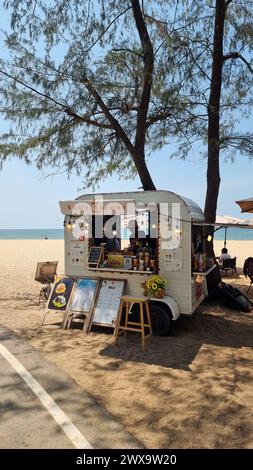 Rayong Thailand 13. März 2024, Ein lebhafter Food Truck parkt an einem Sandstrand neben einem üppigen Baum und serviert Strandgängern unter dem klaren blauen Himmel köstliche Leckereien. Stockfoto