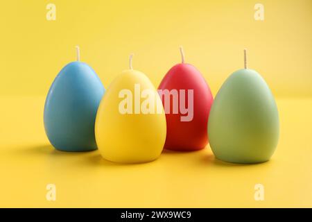 Bunte Kerzen in Eierform auf gelbem Hintergrund. Osterdekor Stockfoto