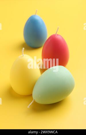 Bunte Kerzen in Eierform auf gelbem Hintergrund. Osterdekor Stockfoto