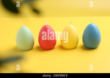 Bunte Kerzen in Eierform auf gelbem Hintergrund. Osterdekor Stockfoto