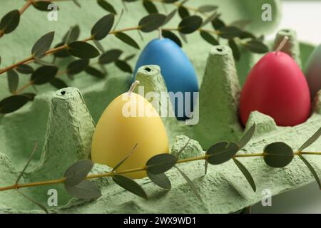 Bunte Kerzen in Eierform im Karton und Blätter auf dem Tisch, Nahaufnahme. Osterdekor Stockfoto