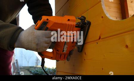 Arbeiten mit einer Stichsäge, um runde Löcher in eine Holzkonstruktion zu schneiden, die Hände eines Arbeiters mit einer elektrischen Maschine, um Kreise in einem Holz zu schneiden Stockfoto