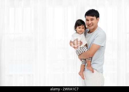 Glücklicher Vater, der Kleinkind auf weißem Fensterhintergrund hält Stockfoto