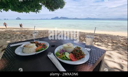 Zwei Teller mit leckerem Essen, wunderschön eingerichtet, auf einem Holztisch am Strand von Koh Kradan Thailand, thailändisches Essen Stockfoto