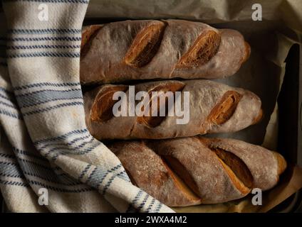 Drei Baguettes auf einer Backform mit Baumwolltuch. In Scheiben geschnittene Brotstruktur Stockfoto