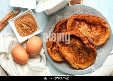 Teller mit traditionellen hausgemachten Torrijas, Zimt, Milch und Eiern auf einem blauen Tisch. Typisches Fastenzeit- und Osterdessert in Spanien Stockfoto