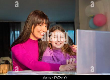 Mutter und Tochter lächeln und schauen sich den Laptop an Stockfoto