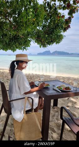 Eine Frau sitzt friedlich an einem Tisch am Sandstrand und genießt den ruhigen Blick auf das Meer und das Rauschen der Wellen. Koh Kradan Thailand Stockfoto